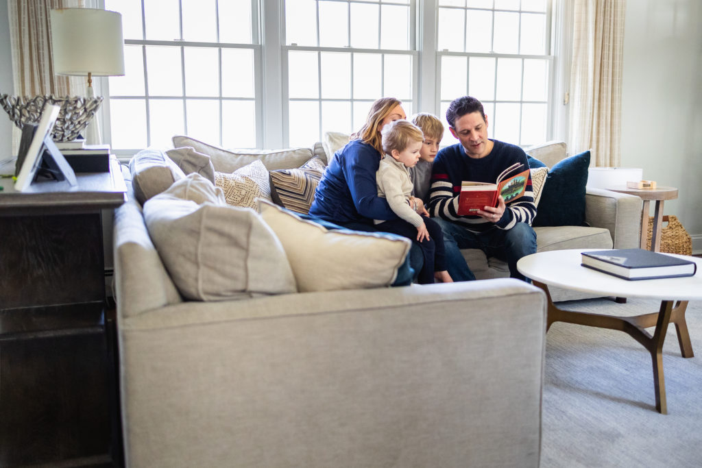 family reading book on couch during in home family photography session in long island